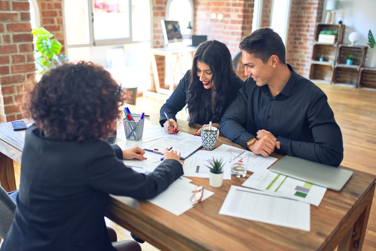 Young couple applying for mortgage. Sitting smiling happy meeting with banker signing papers